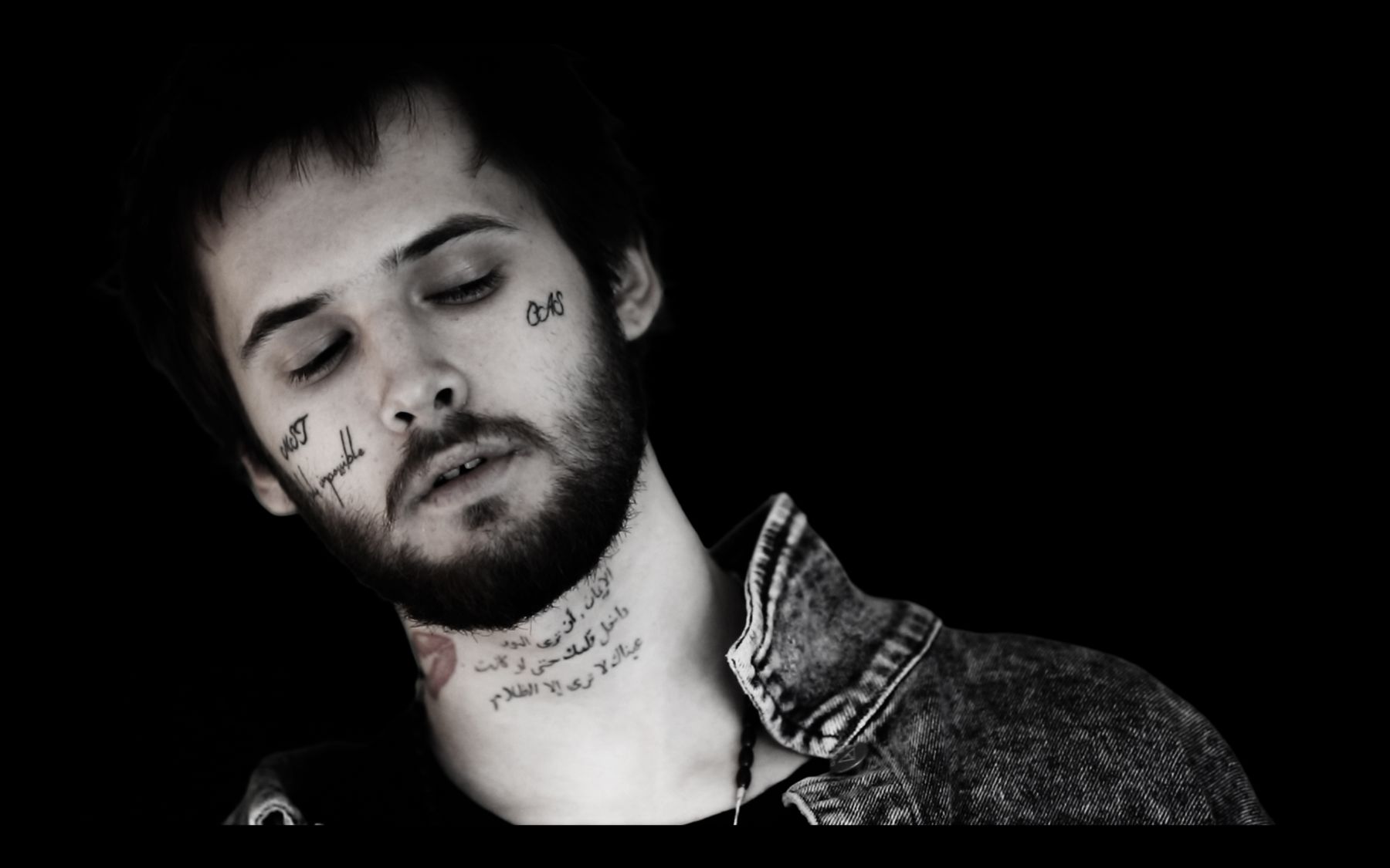 Black-and-white close-up portrait of a tattooed hip-hop artist against a dark background