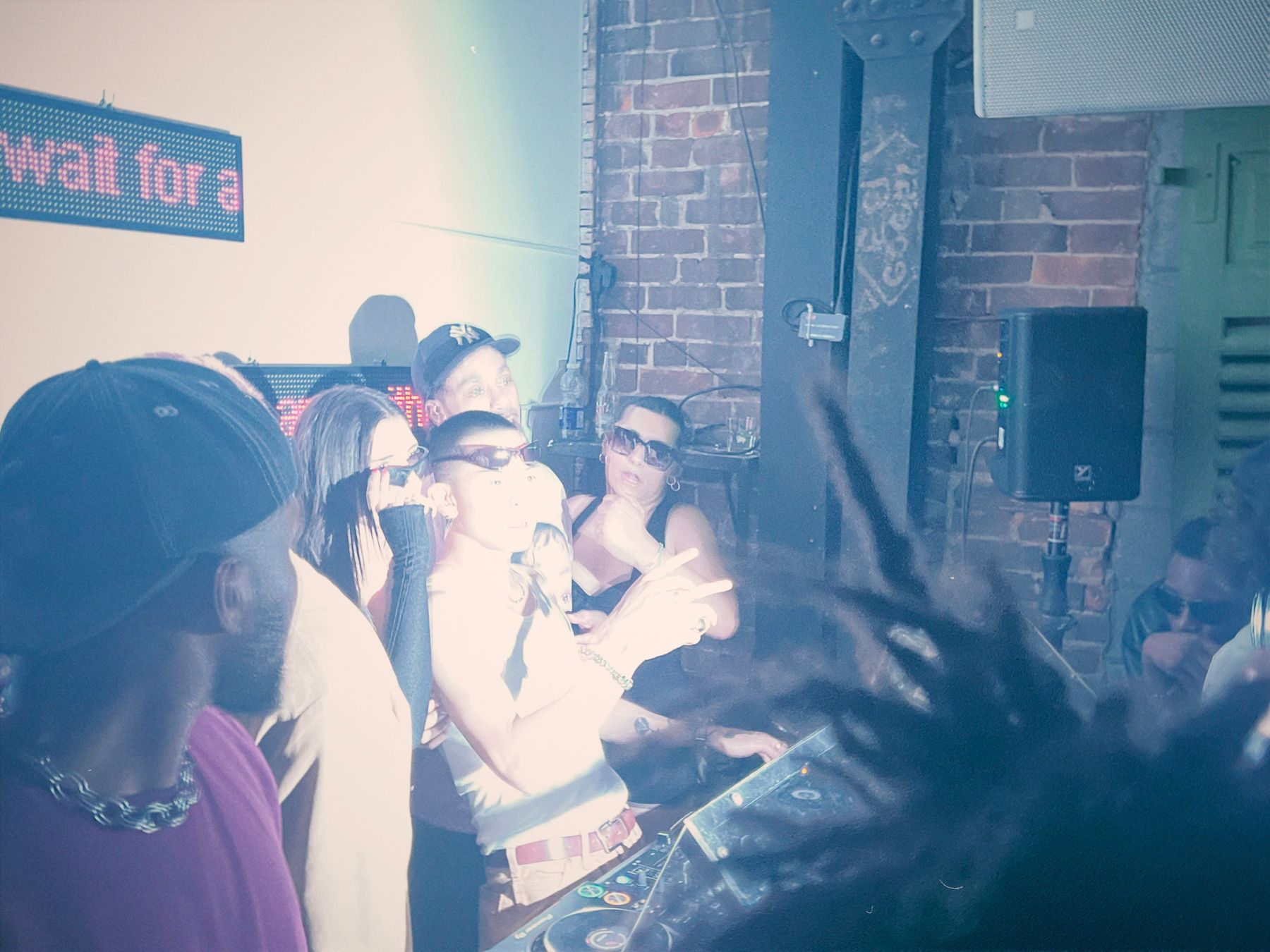 Candid nightclub party scene around a DJ booth under cool lighting